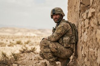 Soldat en tenue militaire complète accroupi près d'un mur de pierre lors d'une mission extérieure en terrain aride